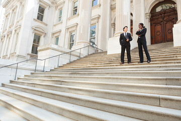 A well dressed man and woman converse on the steps of a legal or municipal building. Could be...
