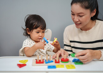 mother teaching her toddler baby girl to playing wooden educational geometric on table