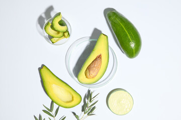 A half of avocado placed on glass petri dish arranged with two petri dishes of avocado cream and...