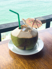 Fresh coconut drink on the wooden table with seascape background. 