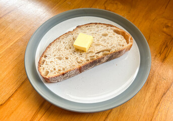 A piece of sliced sourdough bread on top with butter served on the plate.