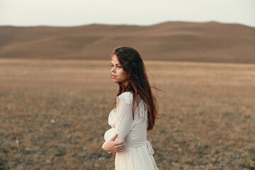 Woman in white dress standing in open field with mountains in background on travel adventure in...