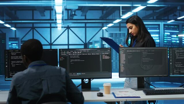 Indian manager in data center doing inspection on electronics and workers, ensuring order. Team leader reading clipboard files, supervising employees in server room infrastructure components