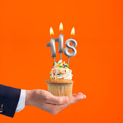 Hand holding birthday cupcake with number 118 candle - background orange