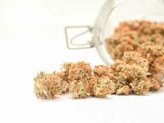 Dry cannabis buds outside of a jar on a white background.