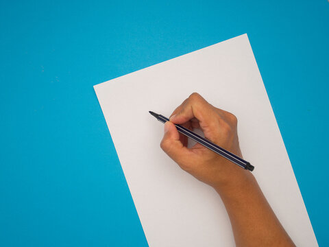 Right hand holding a pen for writing on empty white paper over a blue background.