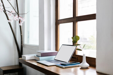 Fototapeta premium Comfortable workplace on wooden counter by the window and laptop, smart phone, note book and pen. vase with small tree inside and a book for read