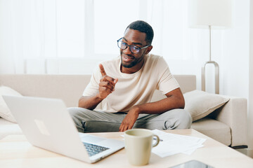 Smiling African American Freelancer Working on Laptop on Sofa in Modern Home The young black guy is...