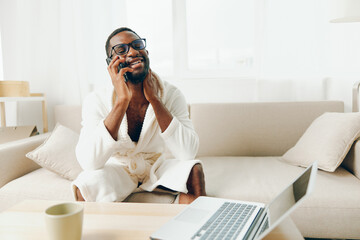 Smiling African American Freelancer Working from Home on Laptop in Living Room, Talking on Phone in...