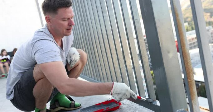 Man paints metal fence with gray paint