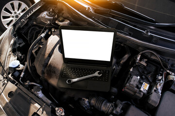 A laptop with a blank white screen and a wrench on a car engine , Car repair and car maintenance servicing concept