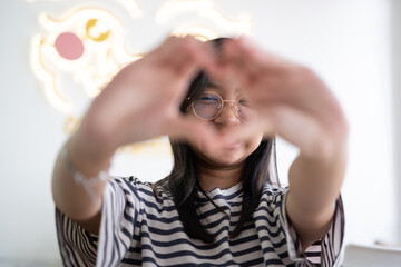 Teenage Asian girl in glasses is making a head shape with her hands with a smiling face.