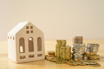 A house model and coins are placed on a wooden table with copy space. Concepts of finance, banking,...