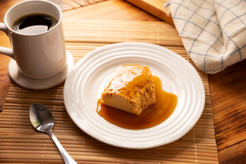 homemade flan dessert, also known as creme caramel, caramel custard pudding or egg custard, served on white plate on wooden table.