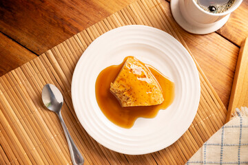 homemade flan dessert, also known as creme caramel, caramel custard pudding or egg custard, served on white plate on wooden table.