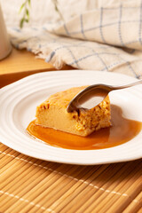 homemade flan dessert, also known as creme caramel, caramel custard pudding or egg custard, served on white plate on wooden table.