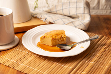 homemade flan dessert, also known as creme caramel, caramel custard pudding or egg custard, served on white plate on wooden table.