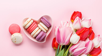 Pastel colorful tulips and vibrant macaroons fill a heart-shaped bowl