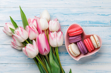 Pastel colorful tulips and vibrant macaroons fill a heart-shaped bowl