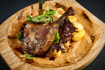 Duck leg confit with baked apples, presented on a wooden cutting board, top view. A delicious...