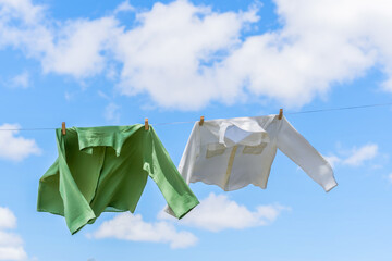 shirts on a washing line drying in the sun moving in the air with a blue sky with clouds in the...