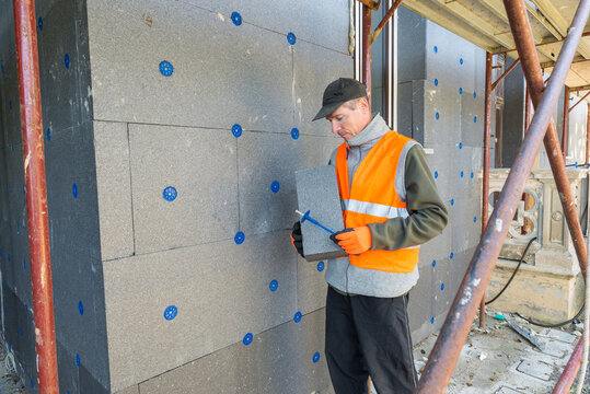 Installation of thermal insulation on the external walls of a house. Thermal coat to improve the energy efficiency of the house. Worker holding a panel of polystyrene thermal cladding 