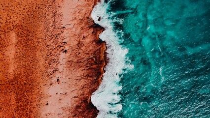 Aerial View of Turquoise Blue Ocean Beach With Crashing Waves and Red Dirt Sand and Rocks © Lauren