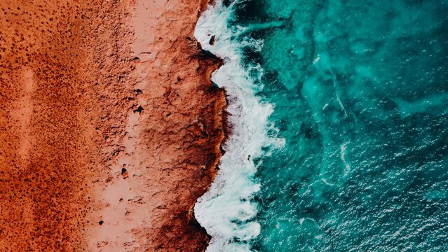 Aerial View of Turquoise Blue Ocean Beach With Crashing Waves and Red Dirt Sand and Rocks