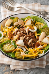 Cheeseburger Salad crisp lettuce topped with seasoned ground beef, cheddar cheese, pickles, onions, and sesame seed croutons closeup on the bowl on the table. Vertical