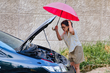 Woman holding red umbrella standing opposite her car with opened bonnet