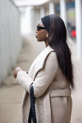 A stylish woman, sporting sunglasses and a headband, stands confidently on the sidewalk, showcasing...