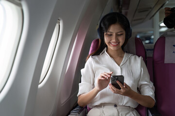 Asian business woman on aeroplane using smartphone
