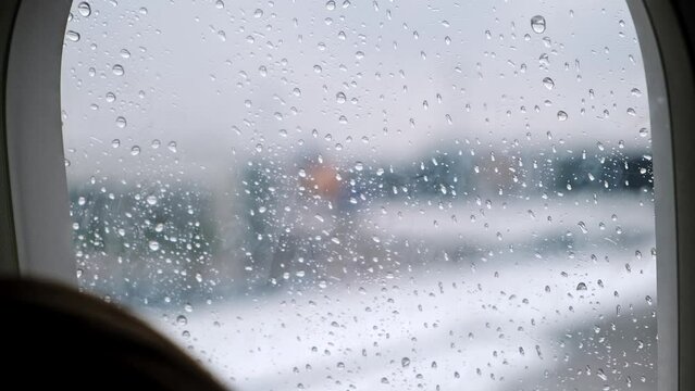 View of raindrops flowing down an airplane window close-up. Rainy weather. Passengers await departure in the aircraft cabin. Departure delayed due to bad weather conditions and poor visibility. 4K