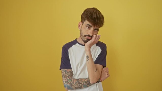Depressed young hispanic man with crossed arms standing isolated over yellow background, looking bored and tired, wrapped in thoughts contemplating his problem.