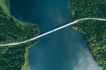 Aerial view of bridge road with red car over blue water lake or sea with island  and green woods in Finland.