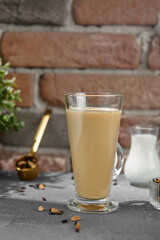 Masala tea on transparent cup. Indian tea with milk and spices on concrete background. Black tea with milk and on upright glass on stone backdrop