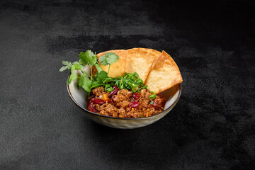 Chilli con carne with beans and corn tortilla on black background. Traditional mexican food - chilli with minced meat and spices in bowl on dark backdrop. Chili con carne in minimal style.