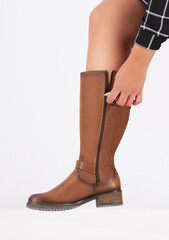 Young woman wearing a stylish brown leather knee-high boot, zipping up the side closure, fine...