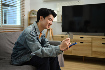 Smiling young Asian man with credit card making financial transaction on smart phone