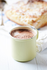 A cup of cocoa with yeast dough in the background. All on a light wooden background. Copy space.

