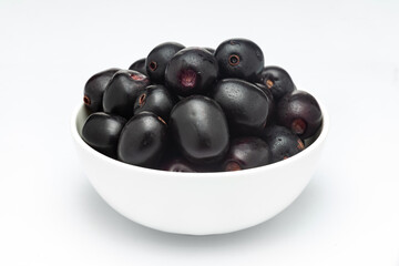 A white ceramic bowl filled with 'Indian blackberry' or Jamun (Syzygium cumini) fresh fruits. Isolated on a white background. Front view.