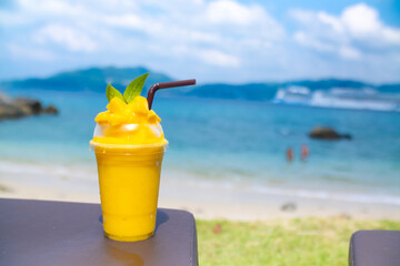 Smoothie made from fresh mango fruits against the backdrop of a seascape. Fruit and yoghurt ice cream decorated with leaves. Glass of tropical dessert close-up.
