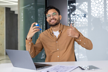 Happy man in office holding asthma inhaler giving thumbs up for asthma relief