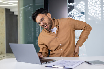 Office worker suffering from back pain while working on a laptop