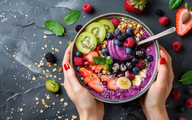 Top-down view of hands holding a vibrant bowl filled with a mix of fresh fruits, granola, and a smoothie