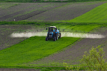 Aerial view of tractor spraying crop in green farm fields with pesticide