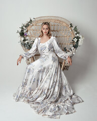 portrait of beautiful blonde female model wearing romantic historical white bridal gown. sitting...