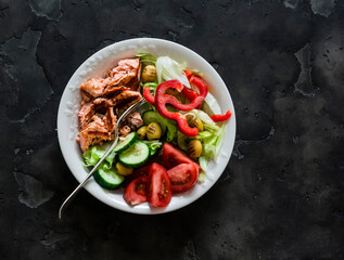 Delicious balanced lunch - grilled salmon, boiled egg, fresh vegetable salad on a dark background, top view