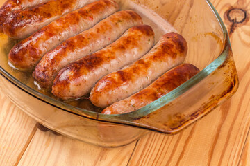 Baked pork sausages on glass casserole pan, fragment close-up