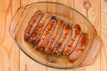 Baked sausages on casserole pan on rustic table, top view